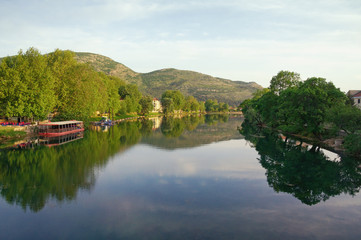 Fototapeta premium Beautiful landscape with calm river, green trees on banks and their reflection in the water. Bosnia and Herzegovina, view of Trebisnjica river near Trebinje city