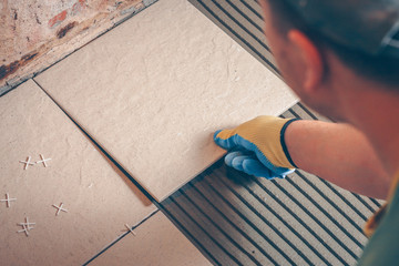 The worker carries out installation of a tile on a floor, finishing and facing works