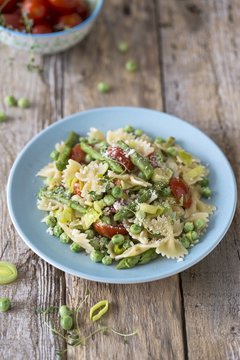Pasta Primavera with asparagus, peas, leek and tomatoes on wooden surface
