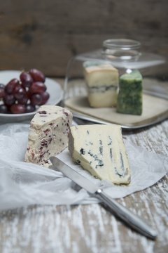 Cambozola and Wensleydale cheese on a piece of paper with a cheese board and grapes in the background