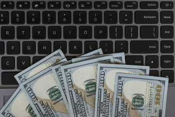 Dollars banknotes and black laptop keyboard as a background. American dollars money. Several hundred dollars bill