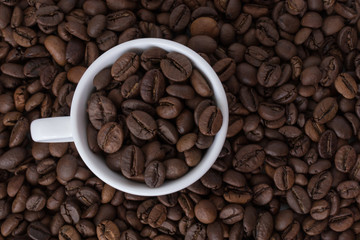 White cup full of coffee beans on the background of coffee beans