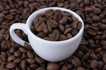 White cup full of coffee beans on the background of coffee beans. Close up