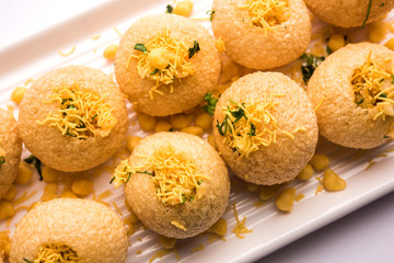 Stuffed Sev Puri is a popular Indian roadside chat item, served in a white plate. Top view, selective focus
