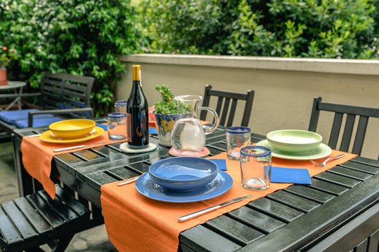 Table set for four diners. Dishes, cutlery and drinks waiting for guests. Waiting for friends for an outdoor lunch. Convivial moments to share with dear friends at home.