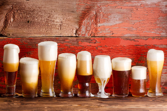 Multiple frothy beer pints on rustic wooden bench