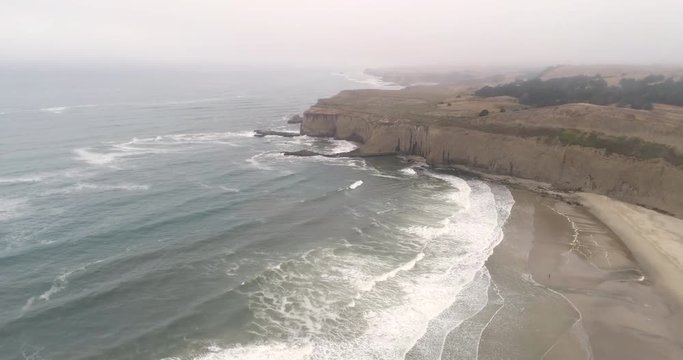 Flight over of steep rocky coastline, waves crashing cliffs - California