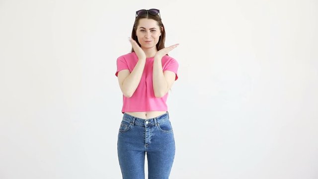 beautiful cheerful girl in sunglasses, pink top and jeans posing against white wall