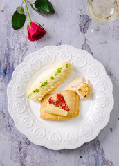 Fried cod fish fillet with mashed potatoes puree and cream sauce on a plate with white wine in a glassand flower rose on background. Heart symbol, date concept, food restaurant menu.