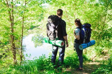 Young couple hikers in forest. sports man and woman with backpacks on road in nature