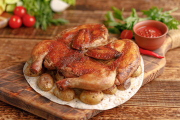 Delicious tobacco chicken on a wooden background with fresh vegetables. Rustic.