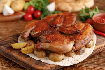 Fried chicken on a wooden background with fresh vegetables and potato garnish.Tsyplenok tobacco. Rustic.