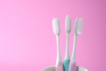 Close-up three white plastic toothbrushes in white mug on pink background