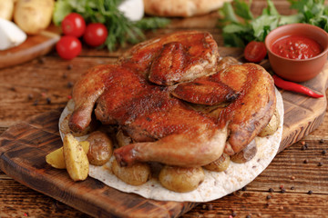 Fried chicken on a wooden background with a garnish of baked young potato. Chicken of tobacco. Rustic.