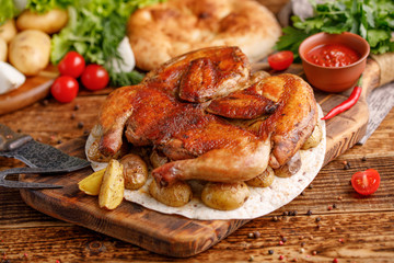 Fried chicken with garnish of baked young potatoes with exquisite appliances. Still-life on a wooden background.