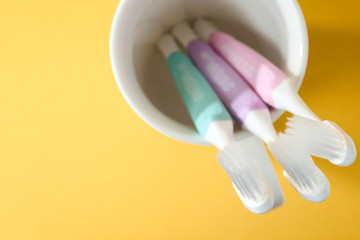 Close-up three white plastic toothbrushes in white mug on yellow background, Seleted focus