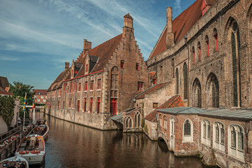Fototapeta na wymiar Old buildings on the canal bank, boats and sunny blue sky in Bruges. With many canals and old buildings, this graceful town is a World Heritage Site of Unesco. Northwestern Belgium.