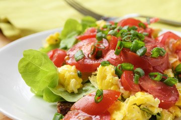 tomatoes on scrambled eggs and green lettuce with chive garnish, close up of a healthy meal