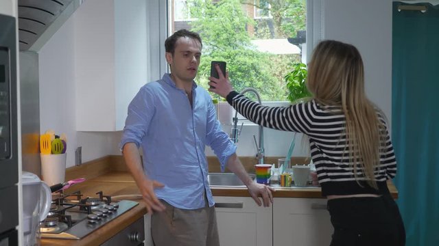 Woman confronts Man about slow motion smartphone text cheating. Slow motion static of young millennial couple having argument about cheating text messages on his phone in kitchen