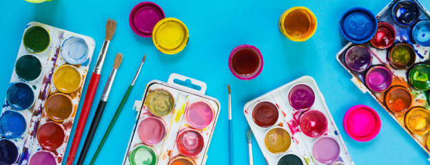 Watercolor paints, artistic brushes,pens accessories for an artist long drawing on a blue background with copy space flatlay top view from above long banner