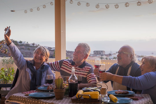 group of adults friends elderly retired having fun taking a picture like selfie all together during a dinner outdoor on the terrace rooftop. celebrate with meal and wine and send memories 