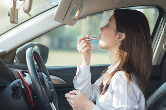 Young woman doing make up in car, painting lipstick