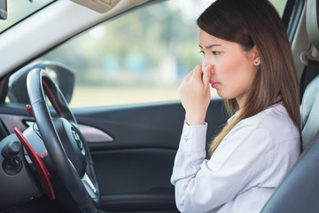 Young woman holding her nose because of bad smell in car.