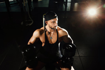 Fototapeta na wymiar Fitness model of a strong man sitting on a bench trains with dumbbells.