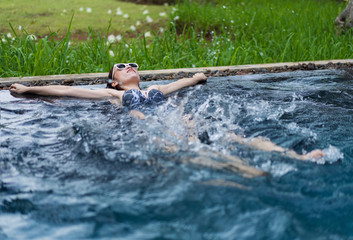 happy woman splashing water by leg in swimming pool