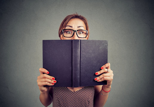 shocked young girl hiding behind an open book