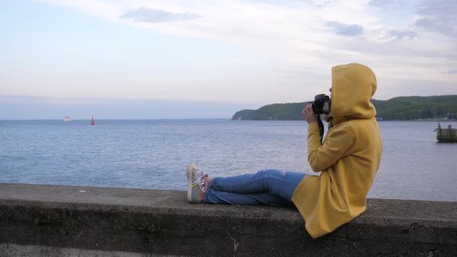 Woman photographer tourist sit on the edge near Baltic Sea bay in Gdynia Poland taking pictures