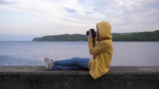 Woman photographer tourist sit on the edge near Baltic Sea bay in Gdynia Poland taking pictures