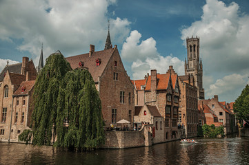 Fototapeta premium Boats and leafy tree with brick buildings on the canal's edge in a sunny day at Bruges. With many canals and old buildings, this graceful town is a World Heritage Site of Unesco. Northwestern Belgium.