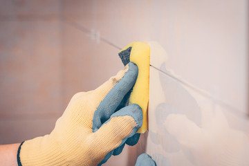 The working tiler wipes the tile on the wall with a damp sponge, removes the glue residues from the intertice seam, the technology of laying tiles and finishing