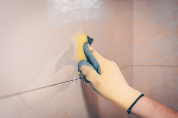 The working tiler wipes the tile on the wall with a damp sponge, removes the glue residues from the...