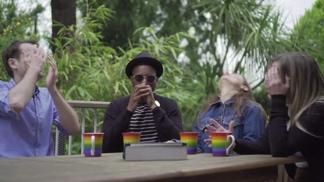 Young group watching game outside disappointed at missed goal. Handheld shot of group of millennial friends with LGBT cups watching sport tablet - disappointed