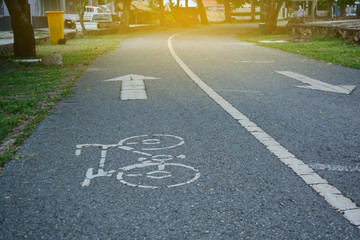 a white sign of bicycle way with arrow direction on the asphalt street at the park in city