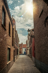 Narrow alley with brick walls and sunshine at City Center of Bruges. With many canals and old buildings, this graceful town is a World Heritage Site of Unesco. Northwestern Belgium. Retouched photo