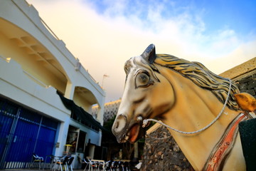 Closeup of yellow toy horse head with expressive face. Evening, yellowish clouds. Room for text. Selective focus.