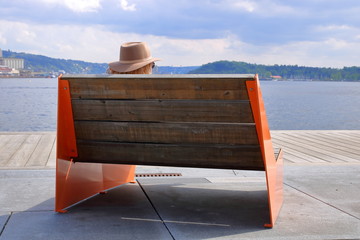 Drewniana ławka z czerwonymi metalowymi bokami, od tyłu, na betonowo-drewnianym nabrzeżu, jakby...