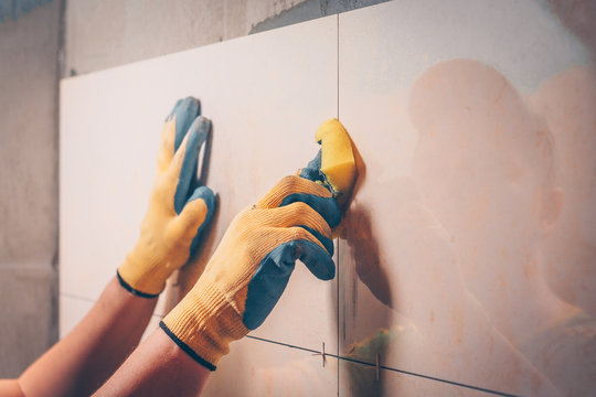 The working tiler wipes the tile on the wall with a damp sponge, removes the glue residues from the intertice seam, the technology of laying tiles and finishing