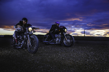 Modern bikers ride on a closed road with helmets on classic motorcycle at sunset. Outdoor portrait and urban lifestyle