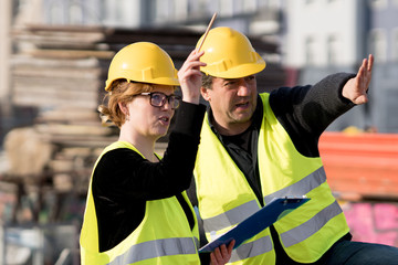 Civil engineers, a man and a woman, wearing safety jackets and helmets, checking projects on...