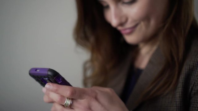 Pretty Business Woman Texting swiping on smartphone and smiling. Handheld close-up of woman texting on smartphone, swiping and smiling