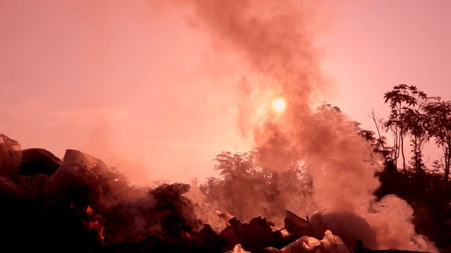 Slow motion fire burning garbage bag on sunrise dark backgorund. White smoke floating to air pollution and dangerous environment. Garbage is waste from comunity. It make green house effect of Earth.