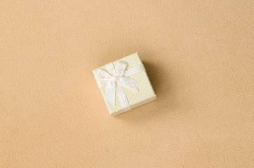 A small gift box in orange with a small bow lies on a blanket of soft and furry light orange fleece...