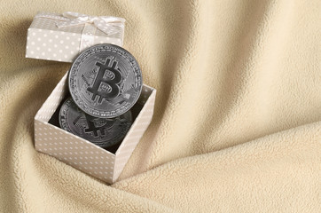 The silver bitcoin lies in a small orange gift box with a small bow on a blanket made of soft and...