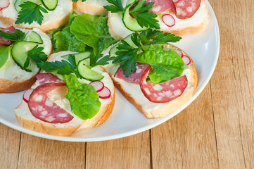 Sandwiches with sausage and greens on a white plate on a wooden table