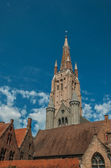 Fototapeta na wymiar Brick church steeple, roofs and public lamp contrasting with blue sky in Bruges. With many canals and old buildings, this graceful town is a World Heritage Site of Unesco. Northwestern Belgium.