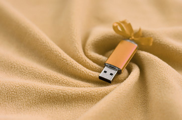 Orange usb flash memory card with a bow lies on a blanket of soft and furry light orange fleece...